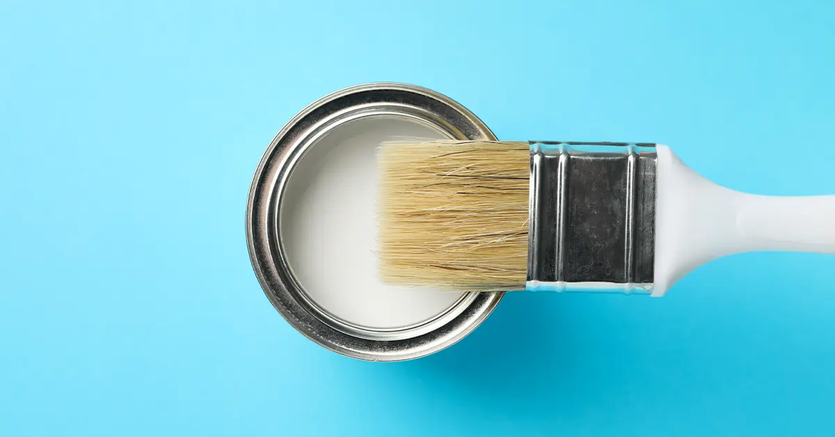 Unused paintbrush on top of can of white paint over light blue background